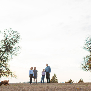 Family stands in silhouette at park with dog