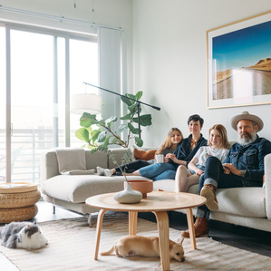 Mom, Dad and two teenage daughters sit on couch next to cat and dog