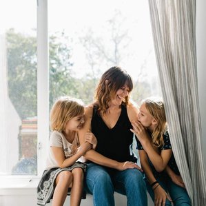 Mother and two daughters sit together smiling in window
