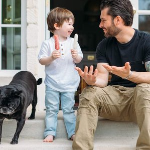 Father and son sit on back porch with popsicles next to puppy