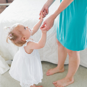 Little girl holds Moms hands in bedroom