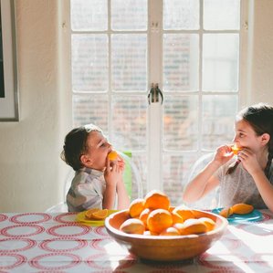 Brother and sister eating oranges in sunny kitchen 