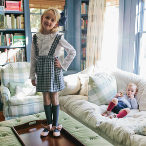 Girl stands on coffee table with brother eats snacks behind her