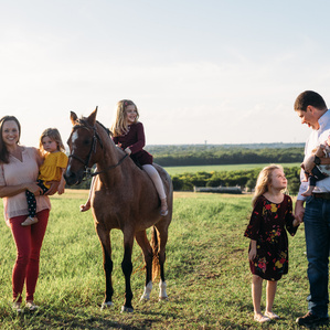 Family of 6 stands in pasture with horse