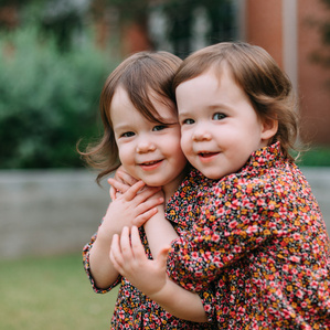 Twin toddler girls in matching dresses hug each other in front yard