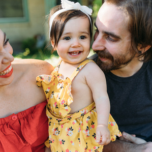 Mother and father sit next to smiling daughter in front yard