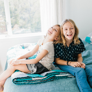 Two young sisters in Austin laughing together on bed