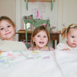 Three sisters play behind bed in room on a rainy day