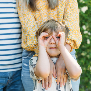 Little boy standing with parents makes pretend binoculars with hands