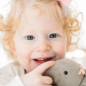 Little girl with red hair and curls cuddles up to stuffed animal