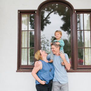 Dad holds son on shoulders while Mom smiles at son laughing