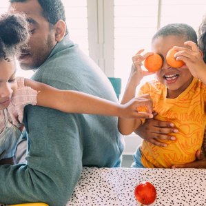 Family sits at dining table together playing with food and being silly
