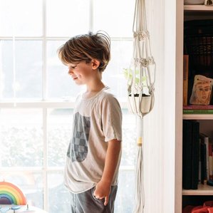 Boy with dimples standing next to sunny window in living room