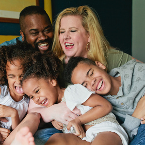 Family sits together on bed laughing together