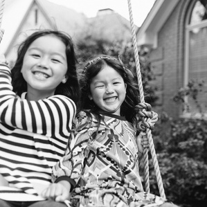 Two sisters on swing smile and laugh