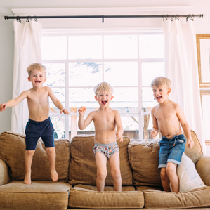 3 shirtless brothers jumping on the couch and laughing