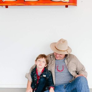 Father and son sit together under BBQ neon sign