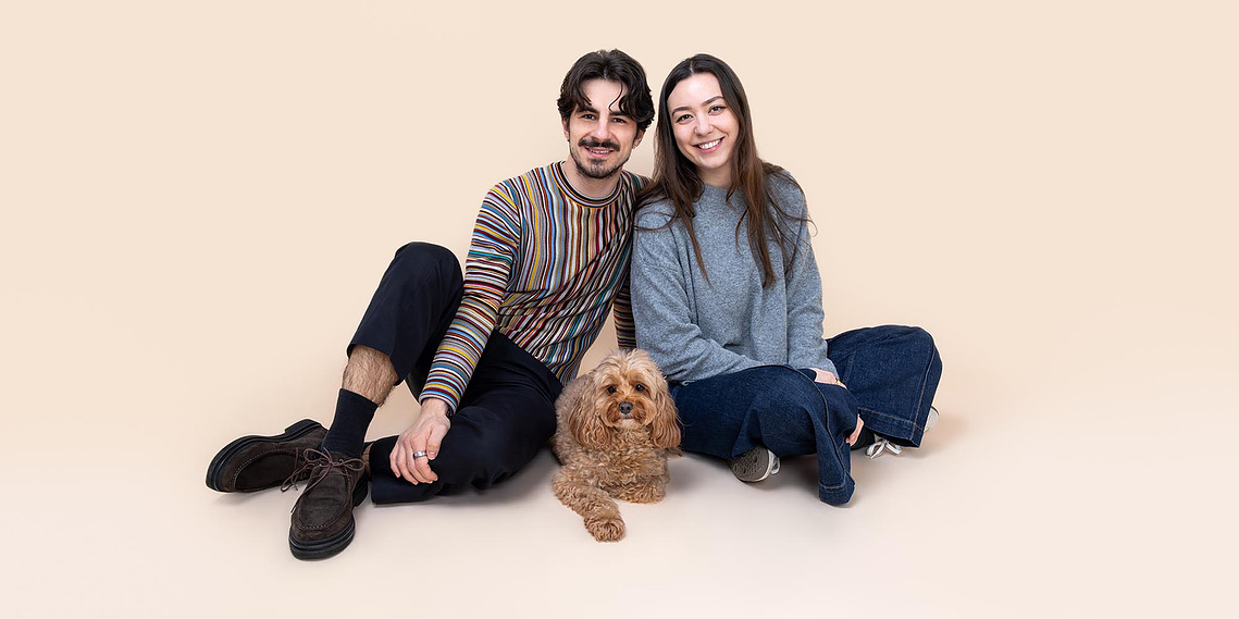 Young couple posing with their Cavapoo - Human and dog studio dog photography in London.  Fun family portrait by Woof Photography. 