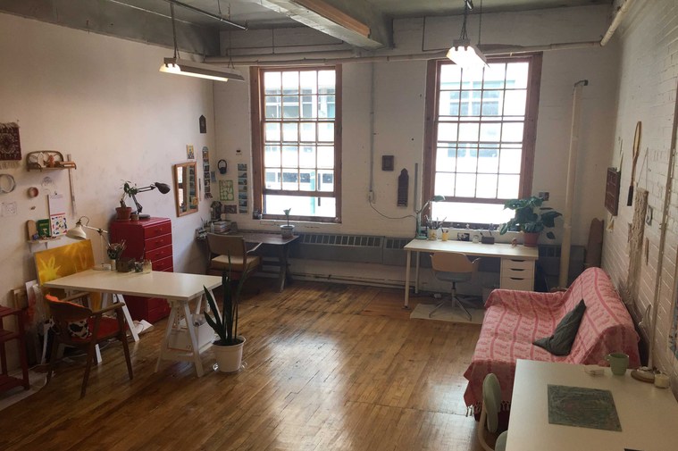 A studio furnished by a couch,table, and chairs lit by windows