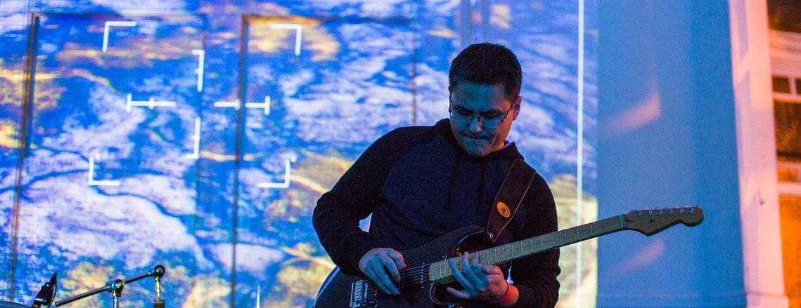 A man plays guitar with exciting projected imagery behind him