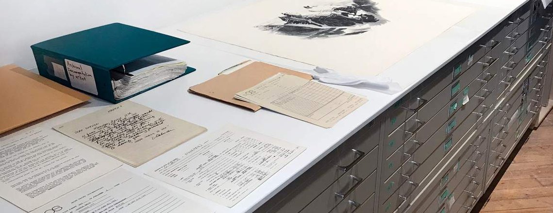 A desk with papers, art and a binder on it. 