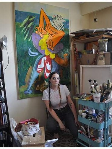 Portrait of artist Charlotte Healey in her studio, sitting next to her supplies and painting