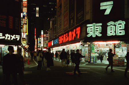 street lit up by neon signs with people walking in the night