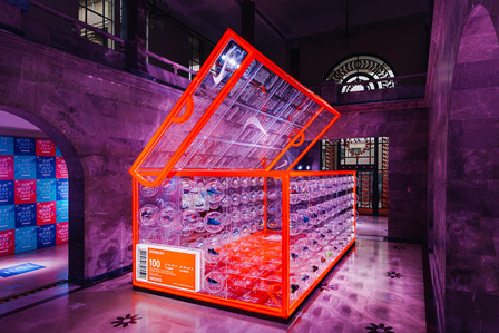 giant orange neon shoebox with transparent plexiglass walls holding bubble-shaped shelves containing nike sneakers. 
