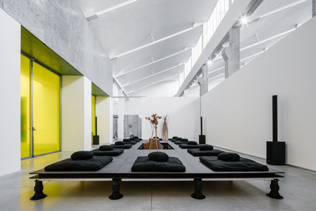 wooden modular meditation platform inside a white warehouse with yellow windows.