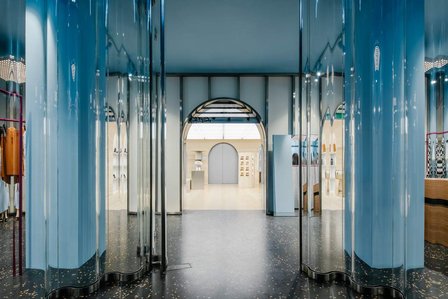 corrugated glass vestibule opening on a black terrazzo floor leading to an arch and a store with travertine walls and floor
