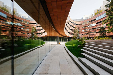 hotel courtyard with stone tiles and steps surrounded by a curved red bricks wall reflecting on a glass wall