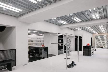 bare concrete interior with shiny metal hangers and black lacquer pieces of furniture. corrugated metal ceiling with neons tubes.