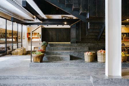 terrazzo steps leading to a sheet metal staircase next to a white beam and fruit baskets inside a super market