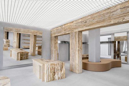 travertine piece of furniture and pillars in a minimalist concrete environment with a large mirror at the back and a custom-made brown sofa.