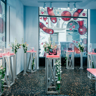 aluminium profile and pink foam cabinets decorated with flower bouquets displaying limited edition handbags, set on a black terrazzo floor. 