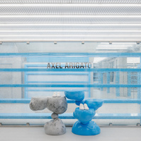 concrete store interior with light blue sculpture display, shelves and a broken glass wall.