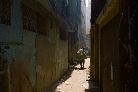 day time, alley way, dark walls, trash, boy, red hat, illuminated scene, pakistan