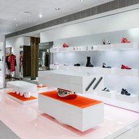 white lacquer custom-made pieces of furniture with orange and stainless steel accents, pink floor and white shoe display wall.