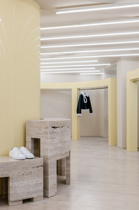 store interior with travertine floor and furniture, glossy yellow pillars and hangers and neon tubes on the ceiling.