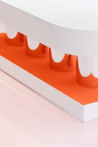 white glossy bench with mirror feet and orange velvet on a pink floor.
