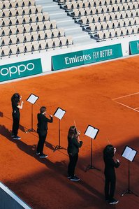 violinists performing on the orange clay of an empty tennis court