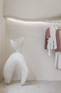 white ceramic sculpture and wall, white metal clothe hanger and terrazzo floor.