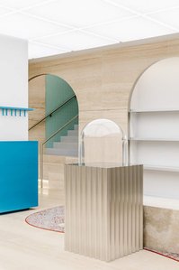 corrugated metal display with a glass dome set on a travertine floor, white pillar dressed in blue metal, travertine arch leading to a staircase made of green tiles