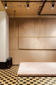marble display with mirror sides set on a wooden checkerboard floor in front of a brown wall and brass rack.