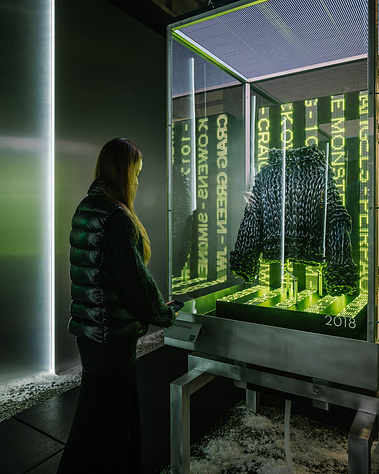 woman admiring a piece of clothing inside a glass and LED screen cabinet