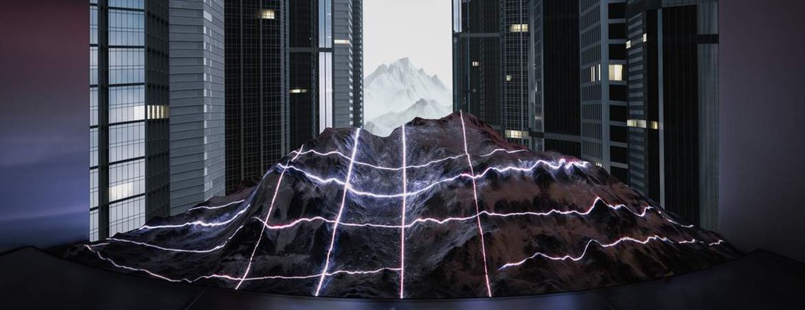 miniature mountain illuminated with a laser grid, set in front of a screen showing skyscrapers