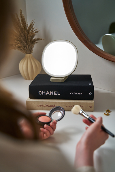 A closeup shot of a Lumie lamp as a woman is using a makeup brush. 