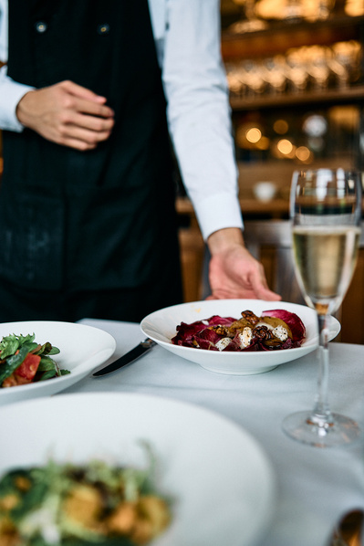 A close up of a waiter placing a meal down at a table in a restaurant. 