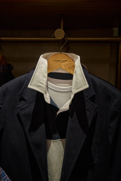 clothes hang on a rack in a dark menswear shop. 