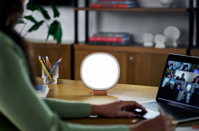 A woman working on a laptop, illuminated by a Lumie lamp. 